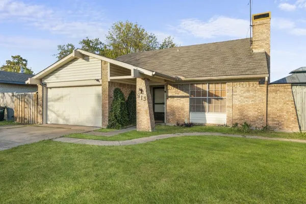 View of front facade with brick siding, a chimney, driveway, and a garage
