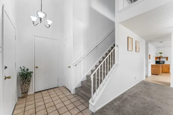 Foyer entrance featuring a towering ceiling, light carpet, light tile patterned floors, a chandelier, and stairs