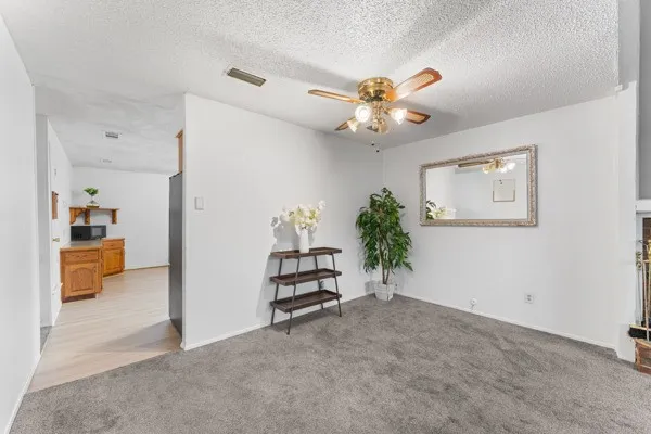Empty room with light carpet, ceiling fan, and a textured ceiling
