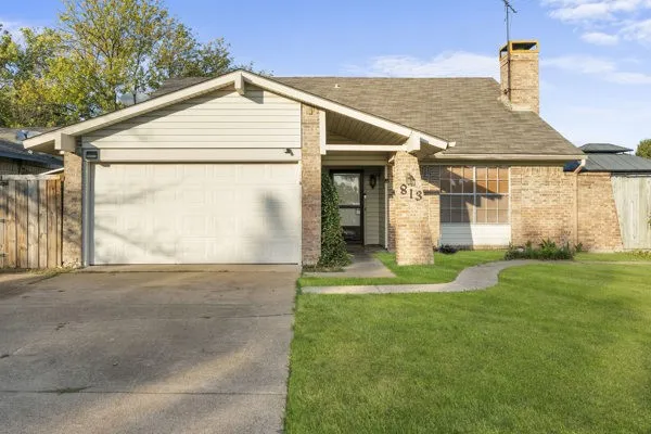 View of front of property with driveway, brick siding, a chimney, a garage, and a shingled roof