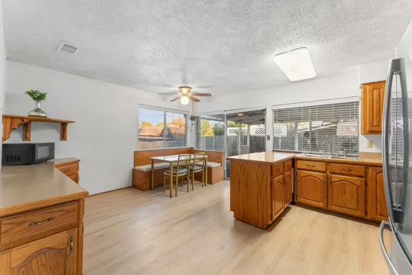 Kitchen featuring light wood-type flooring, light countertops, brown cabinetry, a textured ceiling, and stainless steel fridge