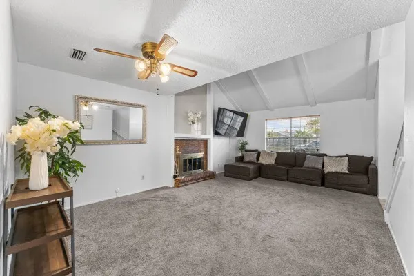 Living area with carpet floors, a brick fireplace, ceiling fan, and a textured ceiling