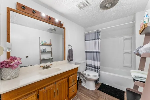 Bathroom featuring a textured ceiling, dark wood-style floors, shower / bath combo, and vanity