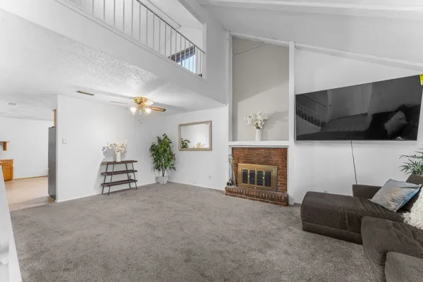Living area featuring carpet flooring, a textured ceiling, a brick fireplace, high vaulted ceiling, and a ceiling fan