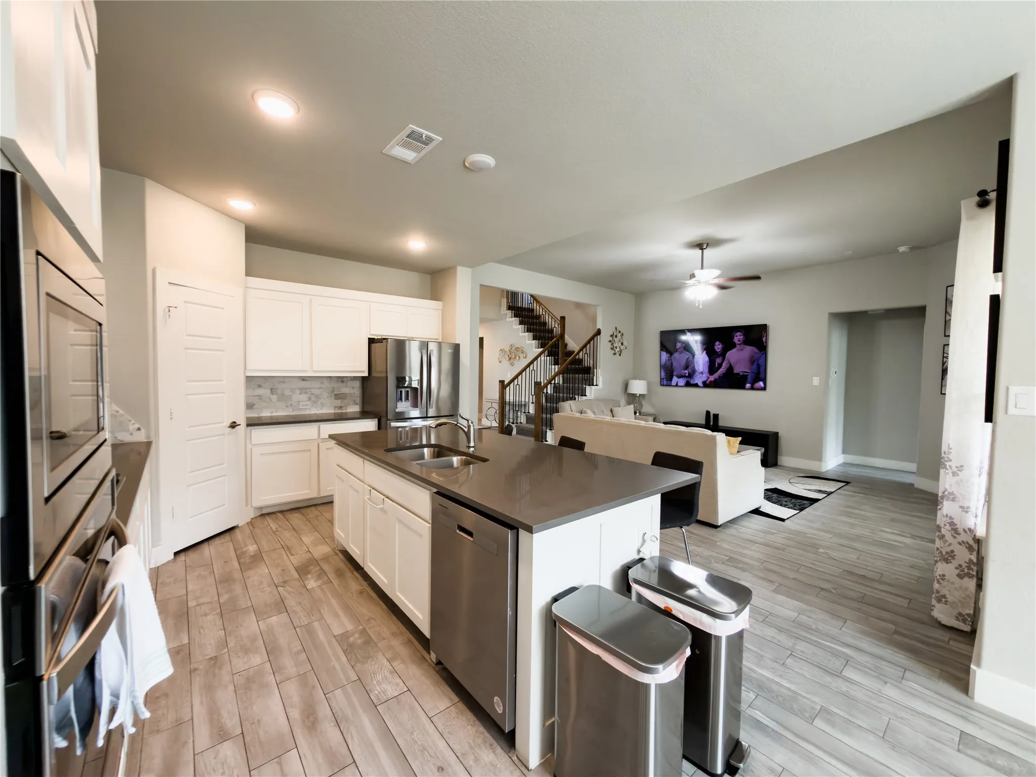 Kitchen with wood finish floors, a kitchen island with sink, stainless steel appliances, open floor plan, and dark countertops