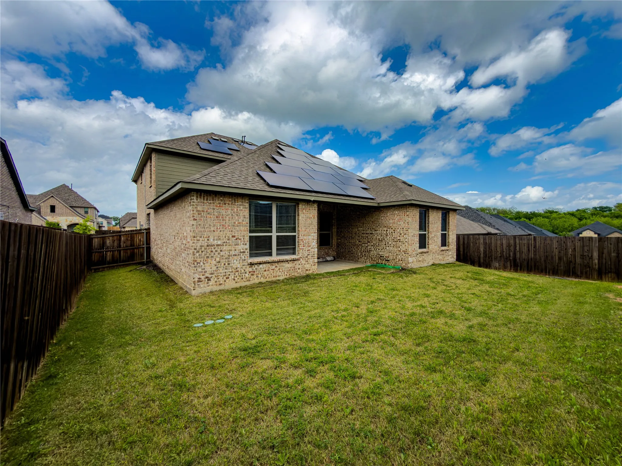Rear view of property with a patio area, brick siding, solar panels, and a fenced backyard