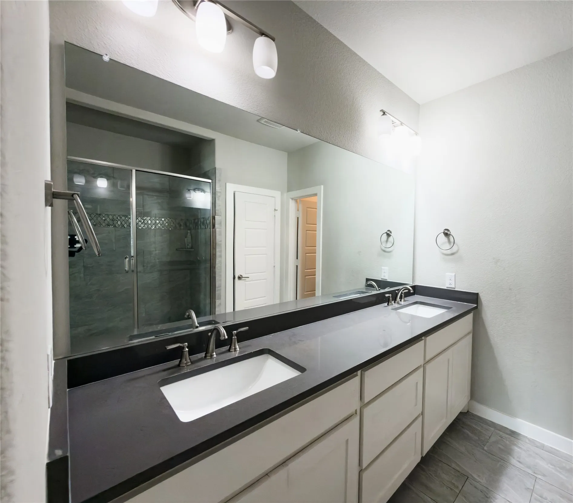 Bathroom featuring double vanity, a textured wall, and a stall shower