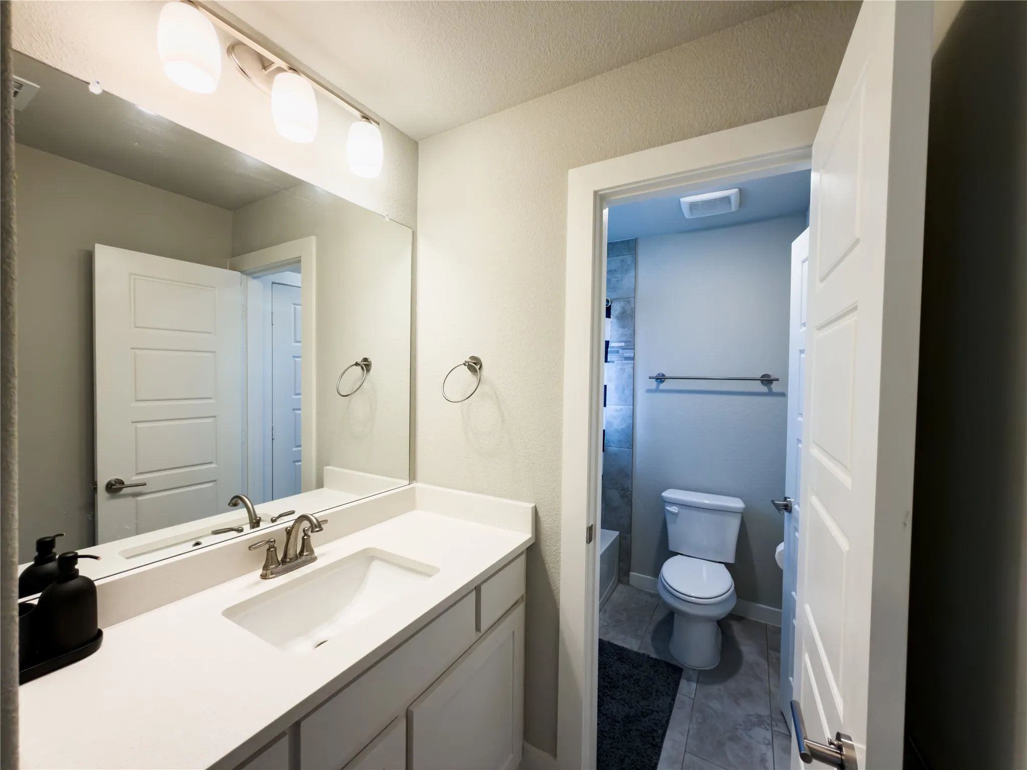Full bathroom featuring vanity, dark tile patterned flooring, and a textured ceiling