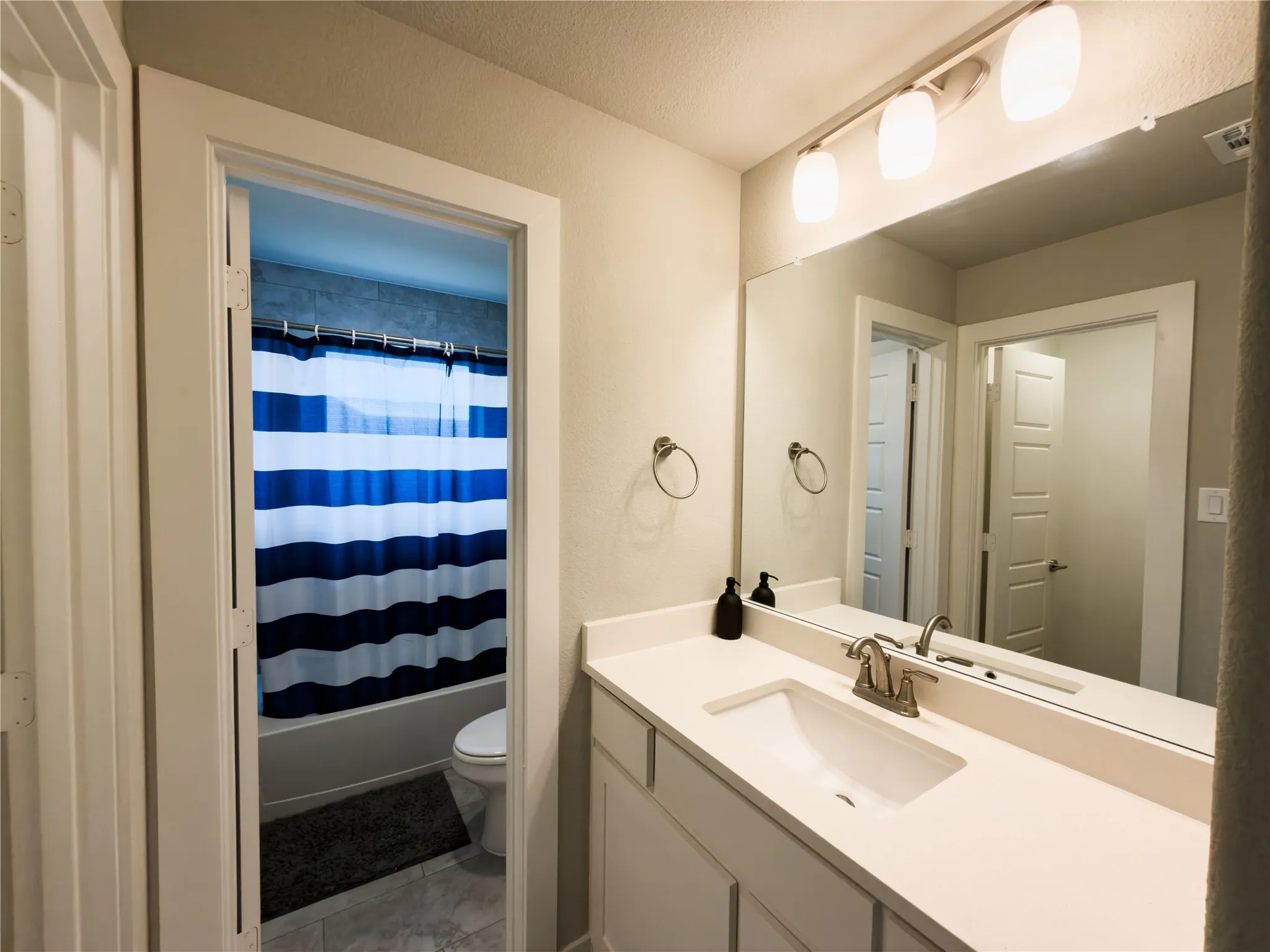 Full bath featuring vanity, shower / bath combo, a textured ceiling, and light tile patterned floors