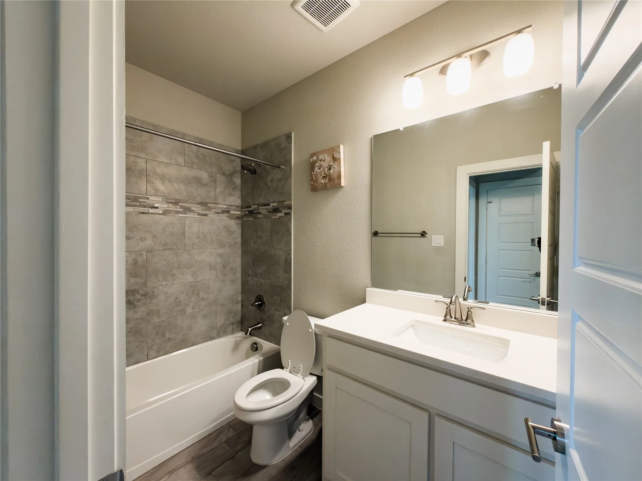 Bathroom featuring vanity,  shower combination, a textured wall, and dark wood-type flooring
