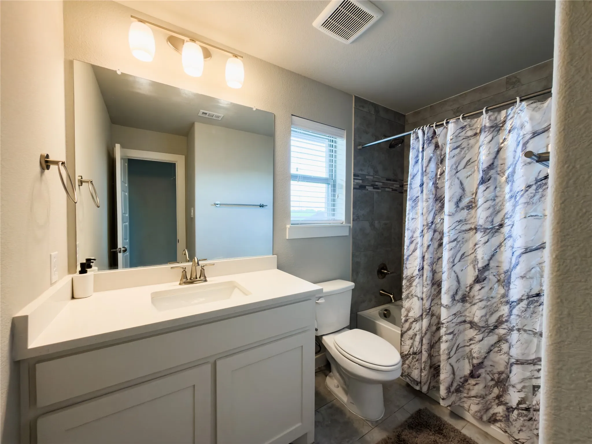 Bathroom featuring vanity, shower / bath combination with curtain, and dark tile patterned flooring