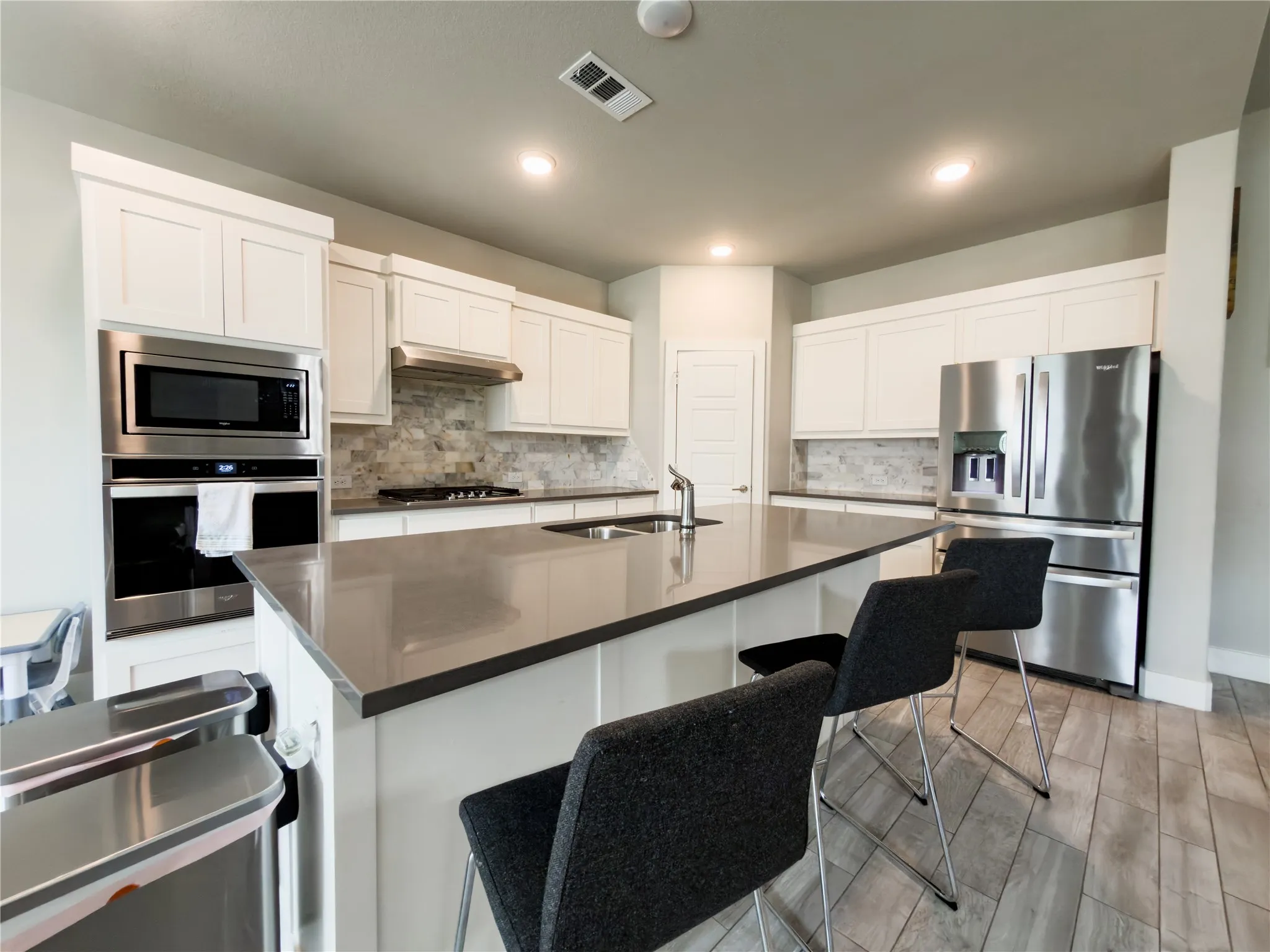 Kitchen featuring stainless steel appliances, wood tiled floors, a breakfast bar, a kitchen island with sink, and white cabinetry