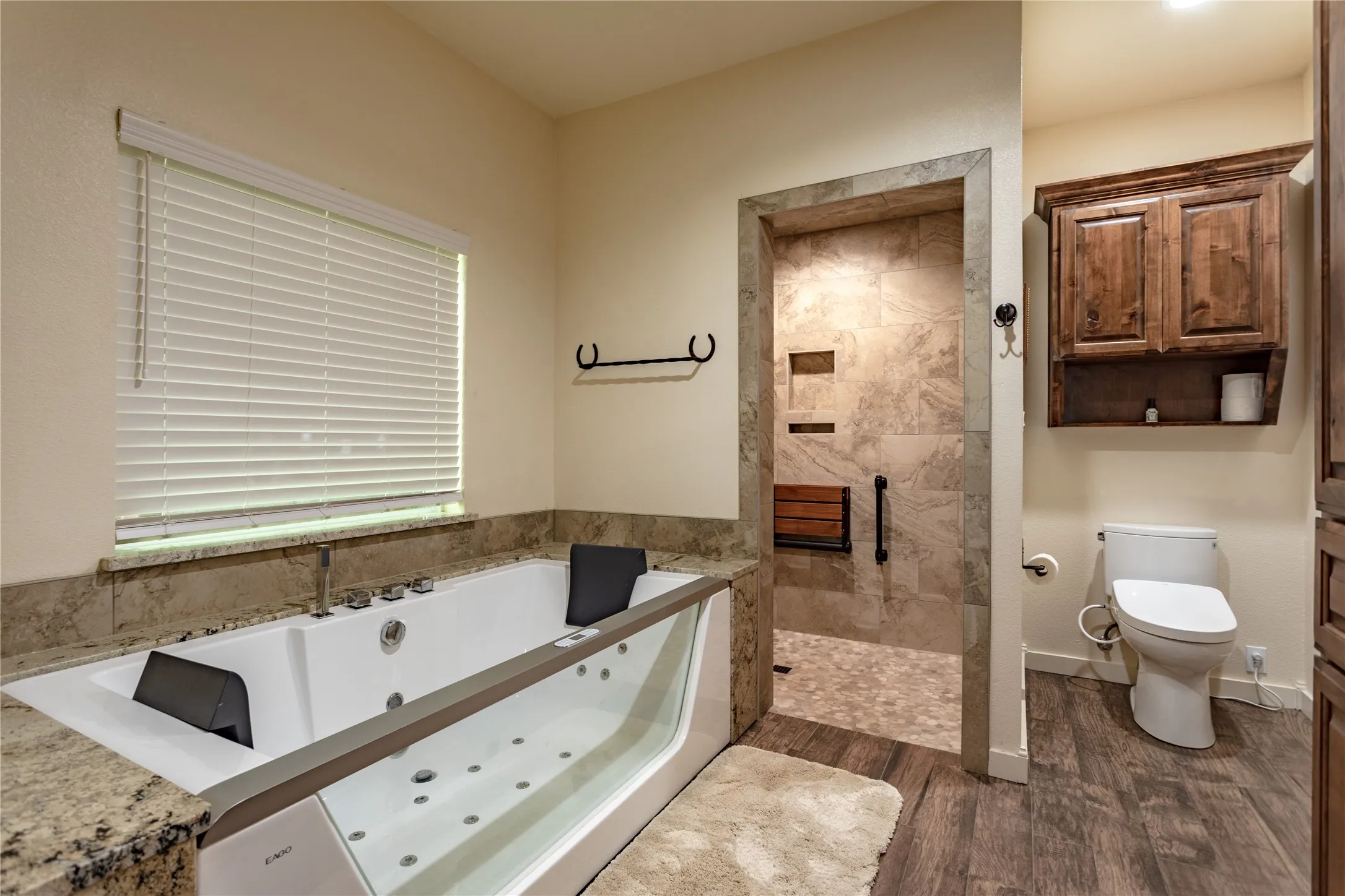 The bathroom features a spacious bathtub with an integrated clear panel and whirlpool jets, set against a granite surround