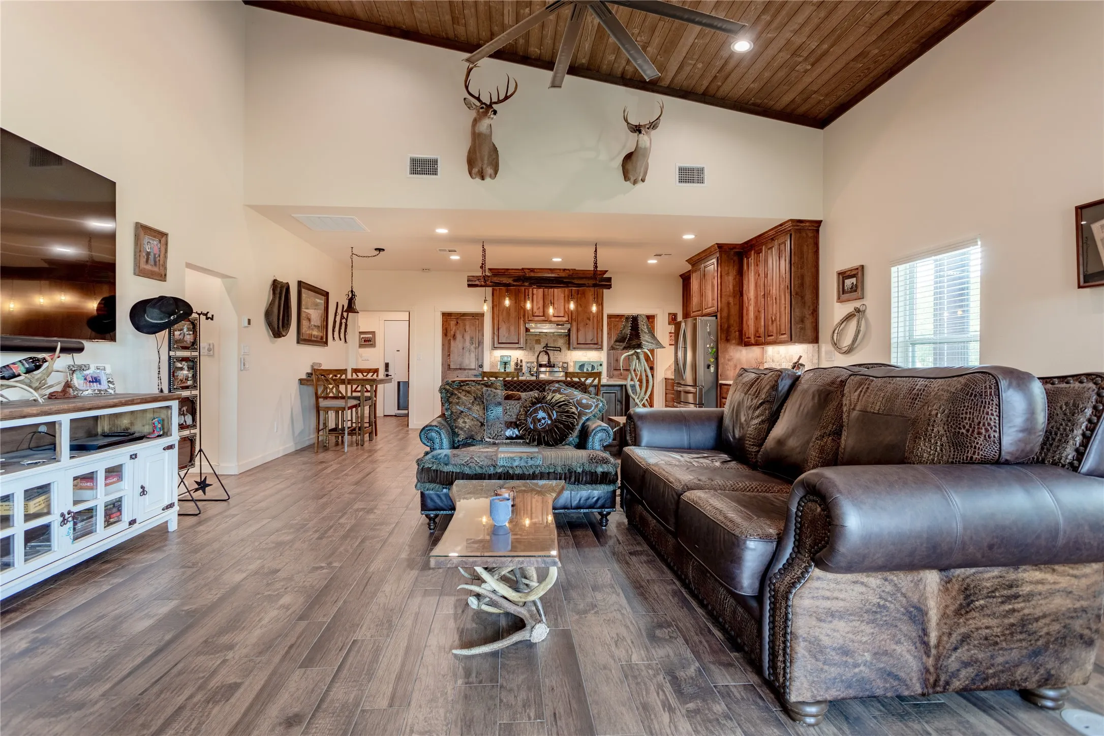 This open-concept living area features a vaulted ceiling with wood paneling and a ceiling fan, wood-look flooring, and recessed lighting