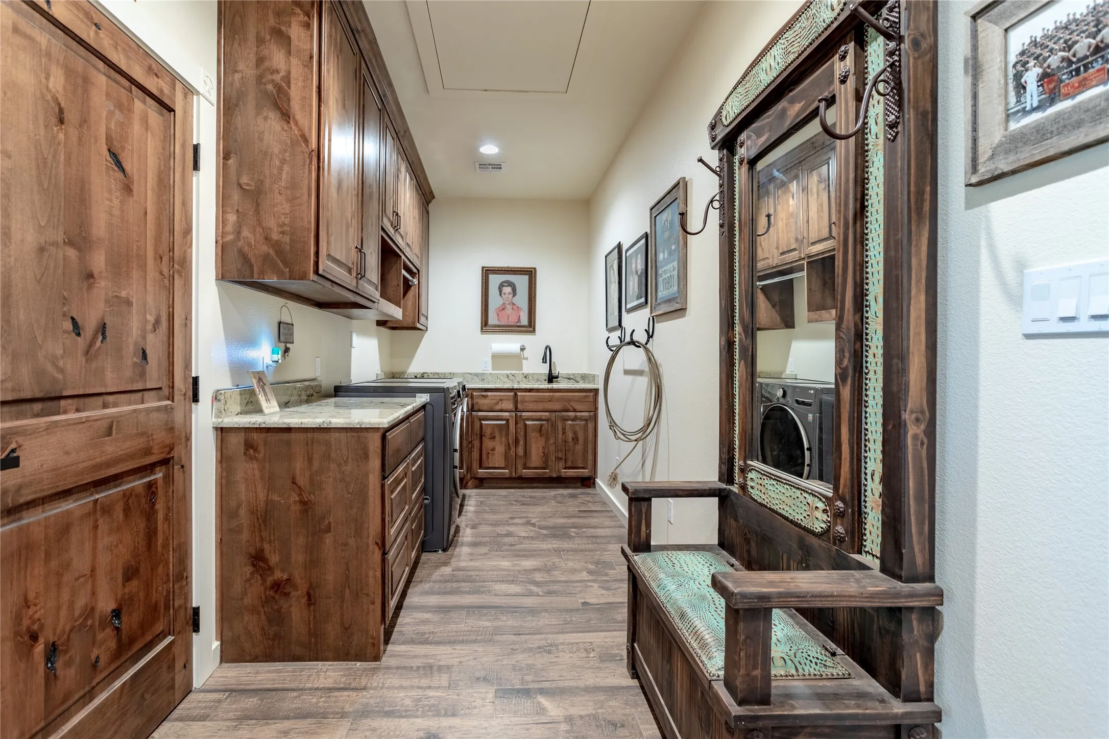 Utility room with wood plank flooring, granite countertops, wood cabinetry, and a built-in washer and dryer