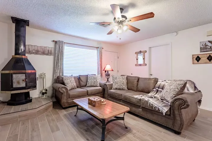Living room featuring wood tiled floors, a wood stove, a textured ceiling, and ceiling fan