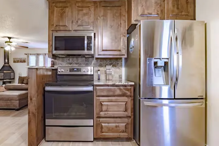 Kitchen featuring stainless steel appliances, light stone counters, a ceiling fan, and wood finish cabinets