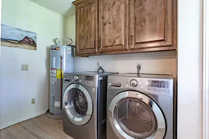 Laundry area featuring electric water heater, separate washer and dryer, light wood finished floors, and cabinet space