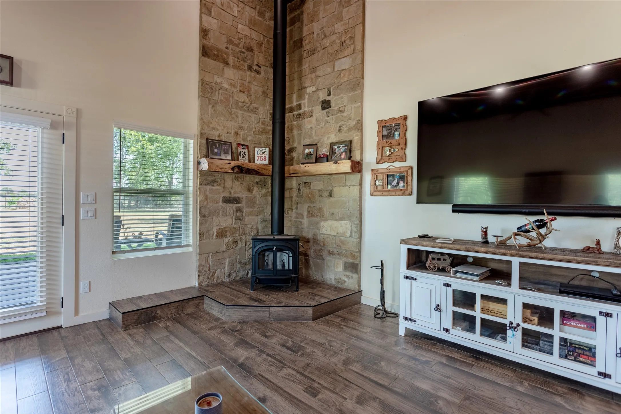 Living area featuring wood-look flooring, a stone-clad fireplace with a wood-burning stove, and a window providing natural light and exterior views