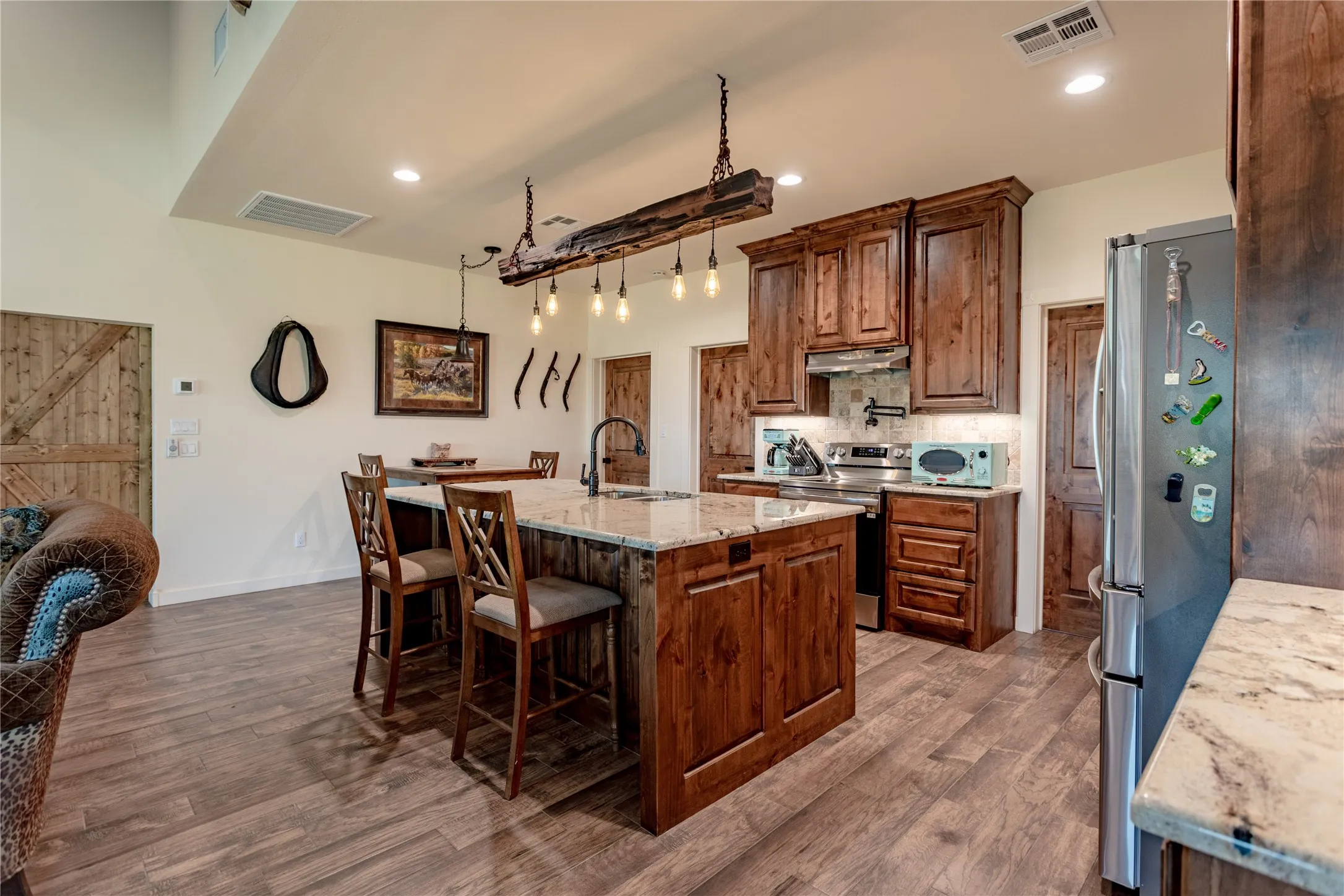 The kitchen features wood plank flooring, a kitchen island with seating, granite countertops, and wood cabinetry