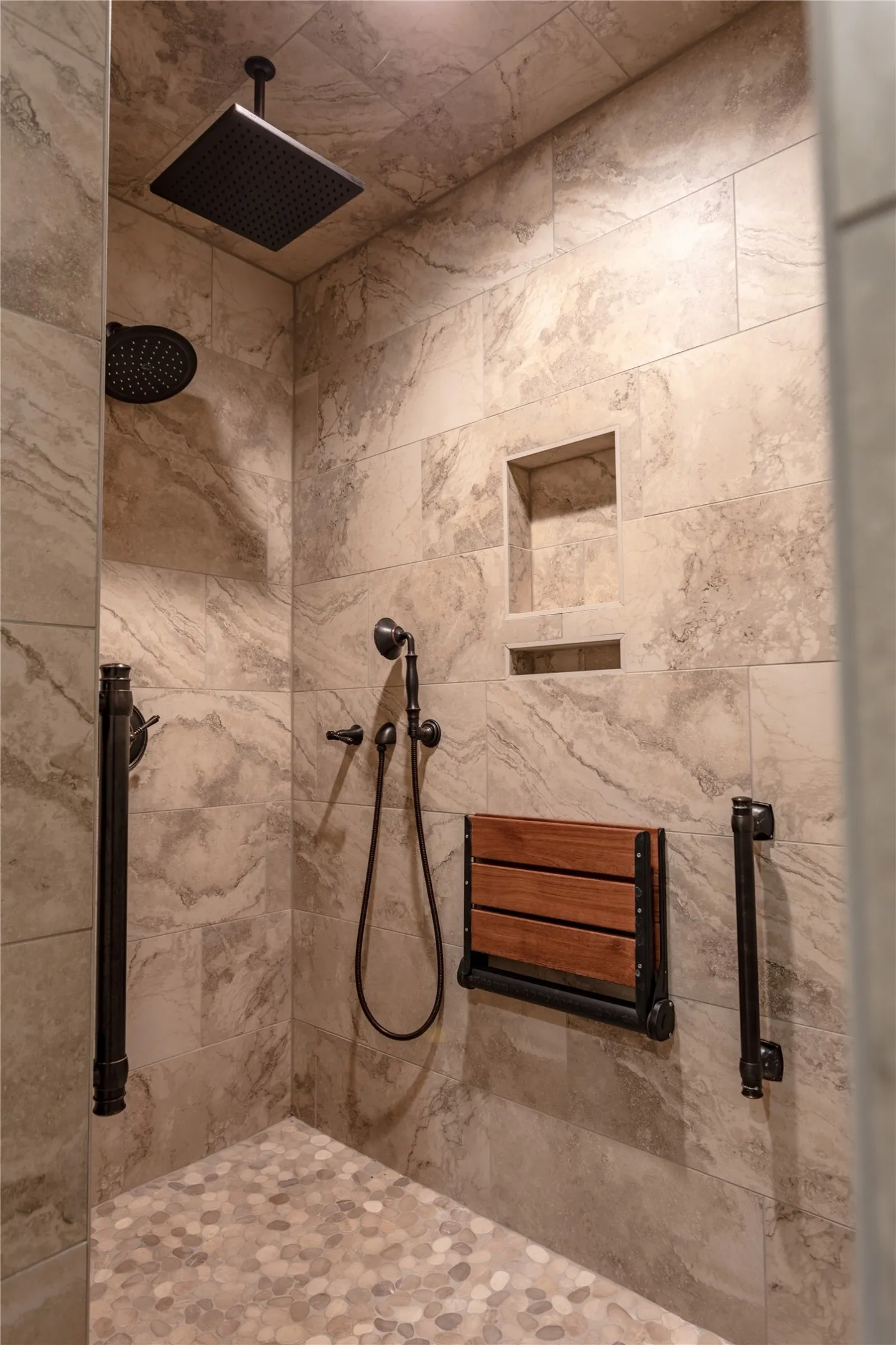 Shower featuring a rainfall showerhead, handheld shower, built-in shelving, and a fold-down wooden bench
