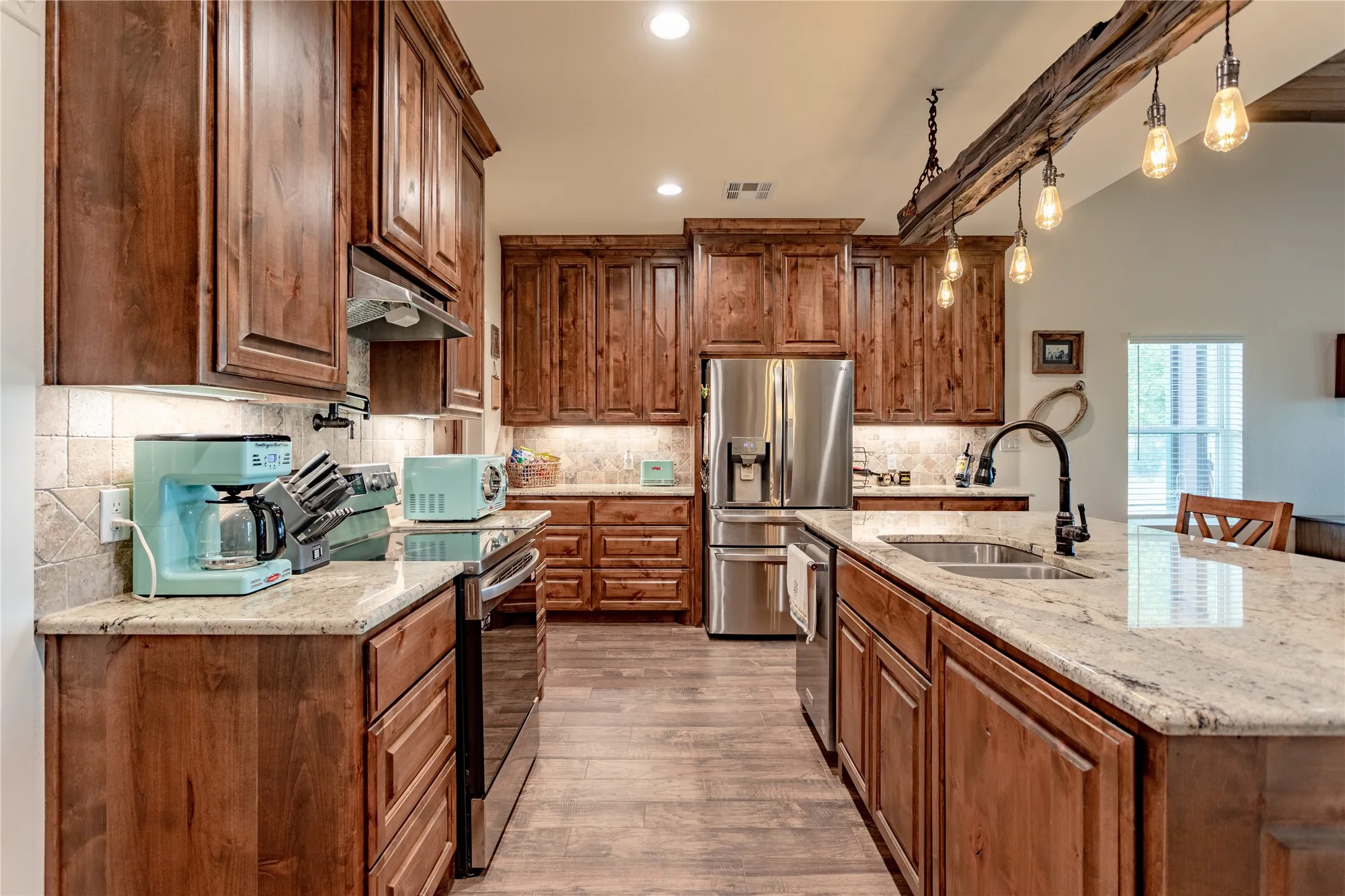 The kitchen features extensive wooden cabinetry, light-colored granite countertops, and stainless steel appliances