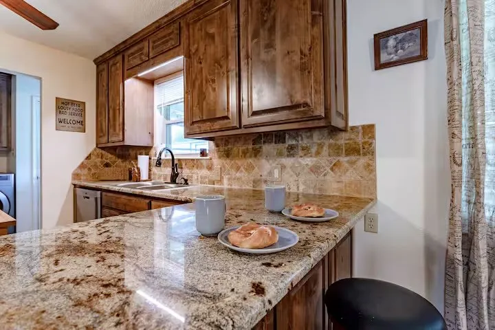 Kitchen with light stone countertops, backsplash, ceiling fan, and dishwasher