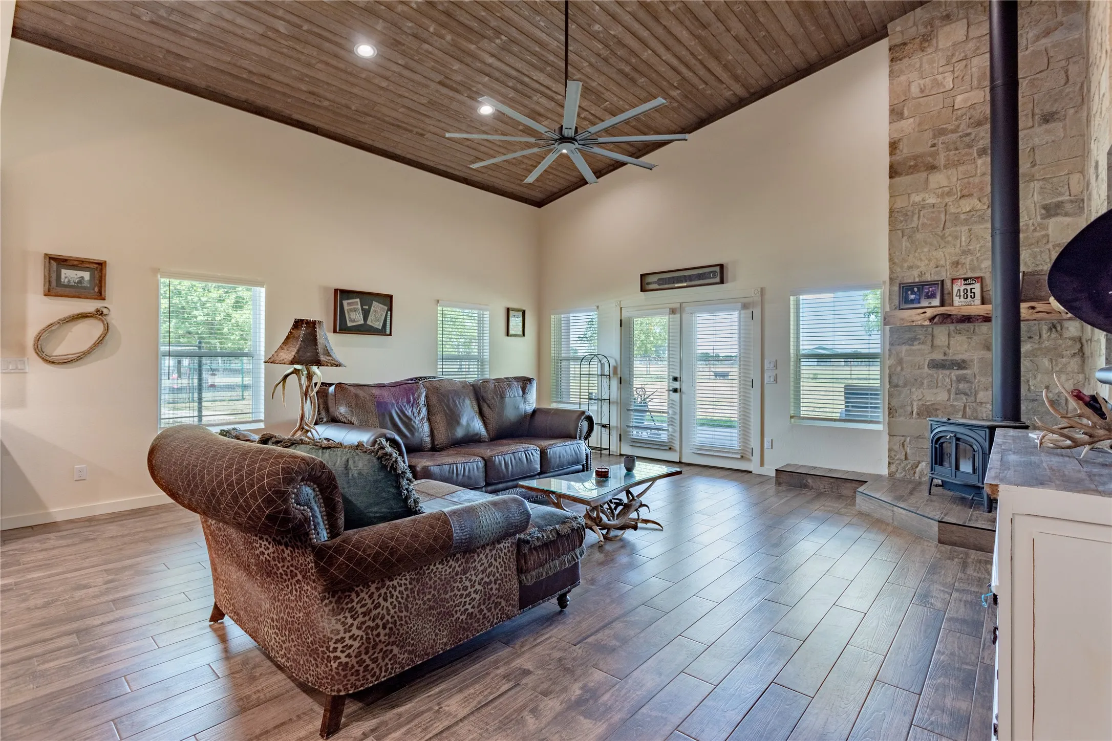 Living area featuring a vaulted wood plank ceiling, a ceiling fan, light wood floors, and a stone-faced fireplace with a wood-burning stove