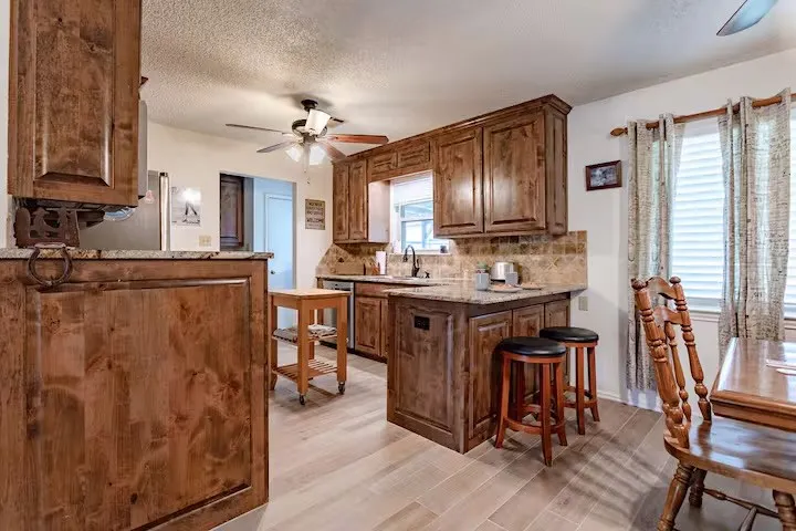 Kitchen featuring ceiling fan, a peninsula, tasteful backsplash, light stone counters, and a textured ceiling