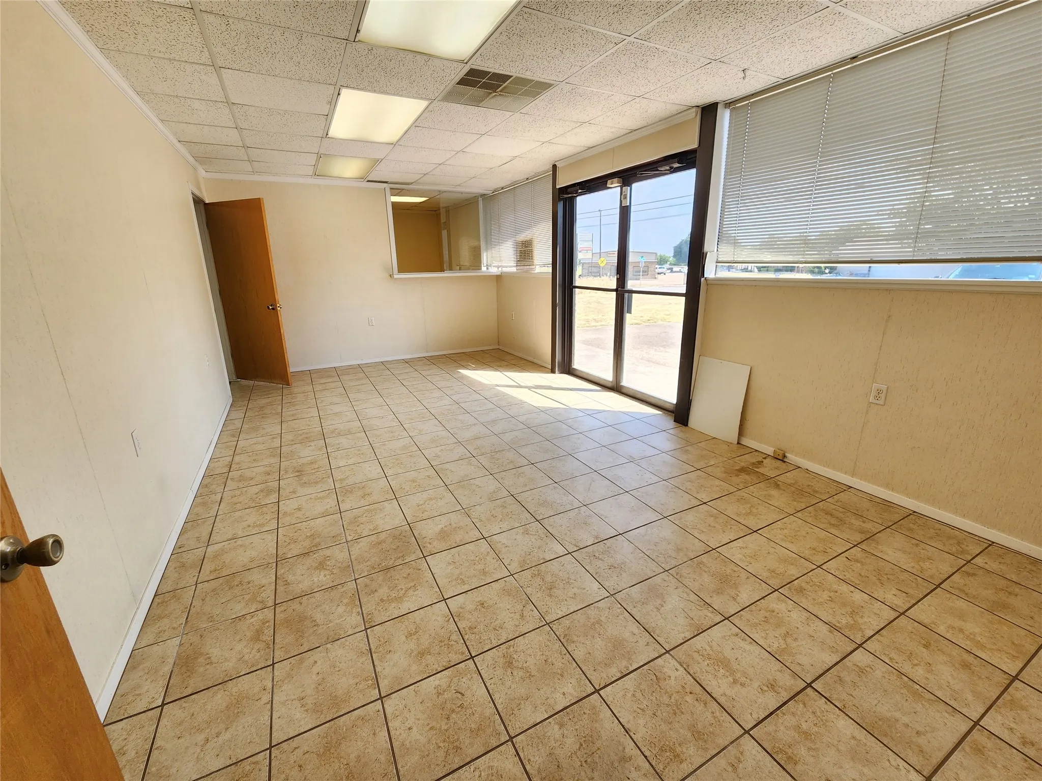 This property features a spacious room with light-colored tile flooring, overhead lighting, and a front entrance with glass doors