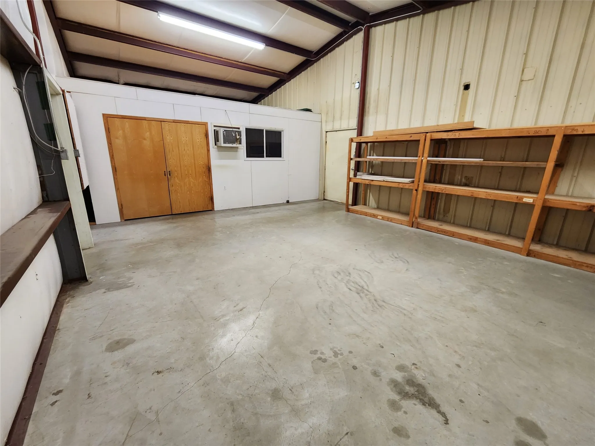 The property features a spacious interior with high ceilings and exposed beams, a concrete floor, and a separate enclosed area with wooden double doors and a window