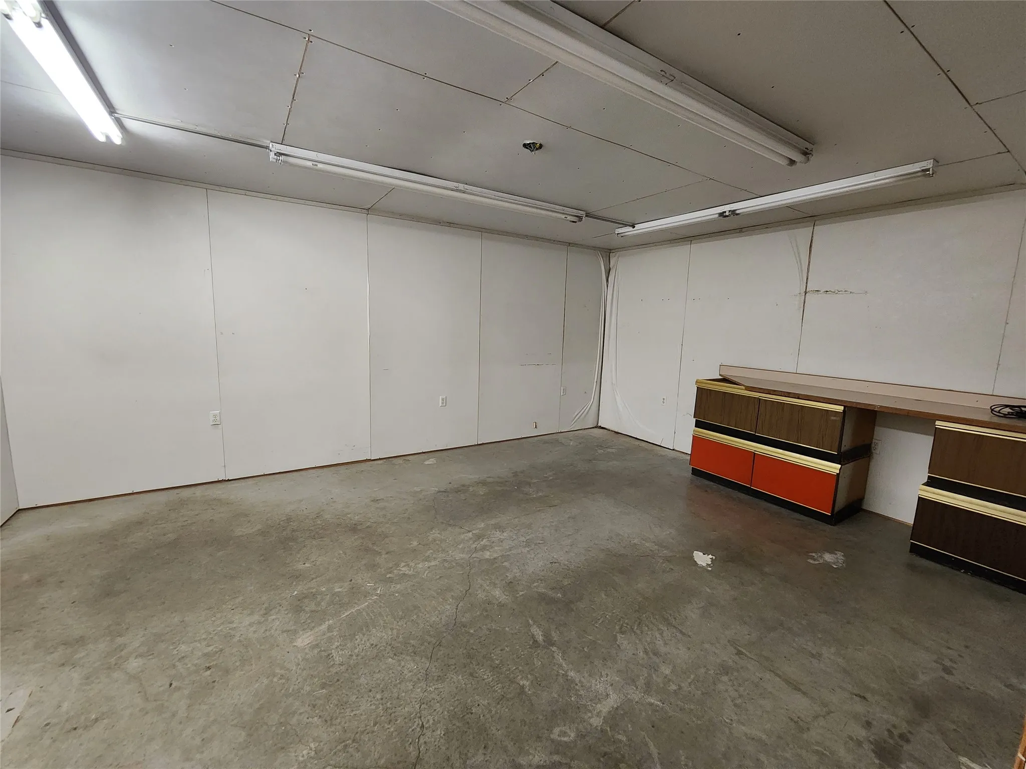 Spacious room featuring concrete floors, white panel walls, and overhead fluorescent lighting