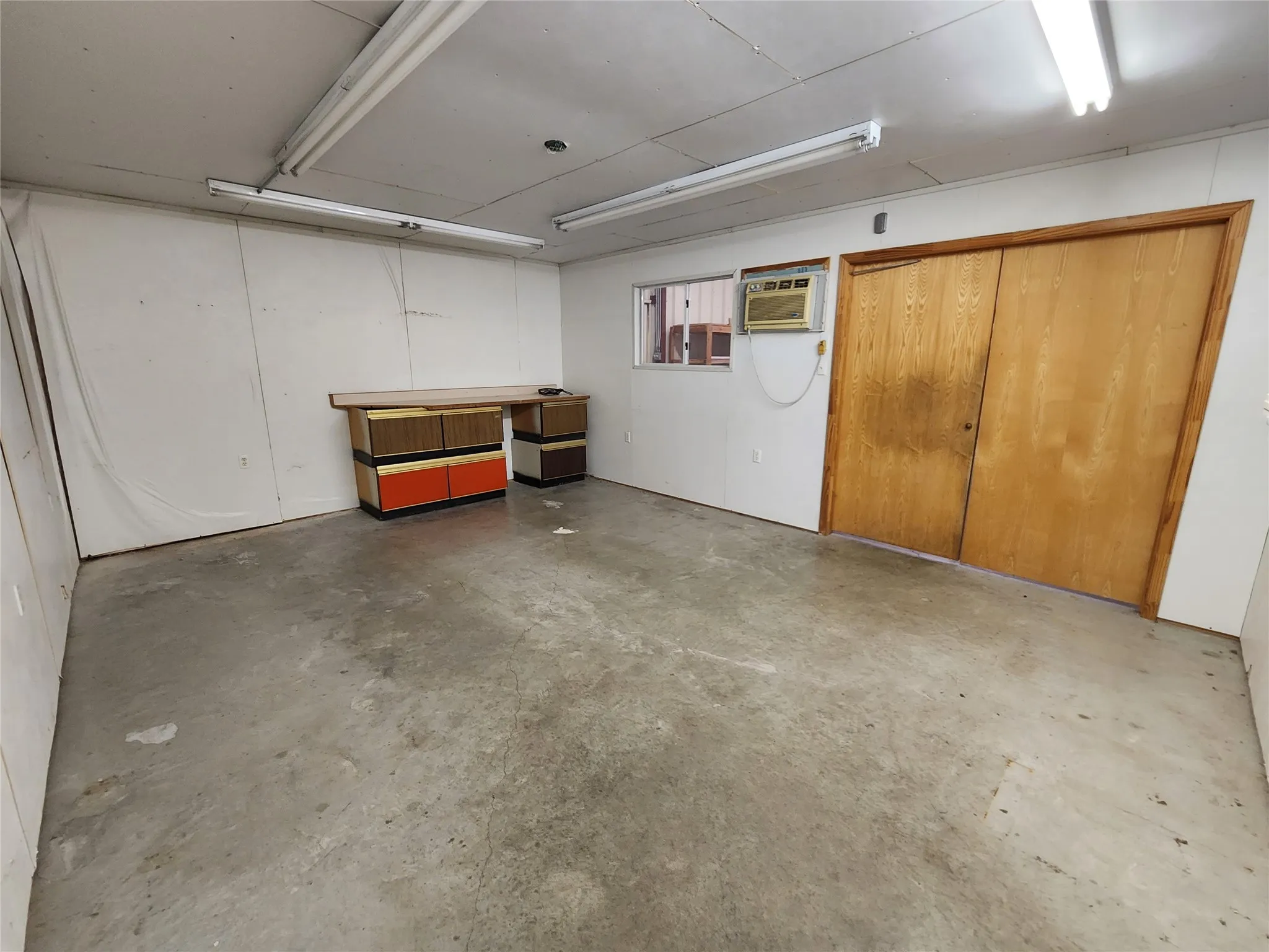 Spacious room with concrete flooring, fluorescent lighting, and a window unit