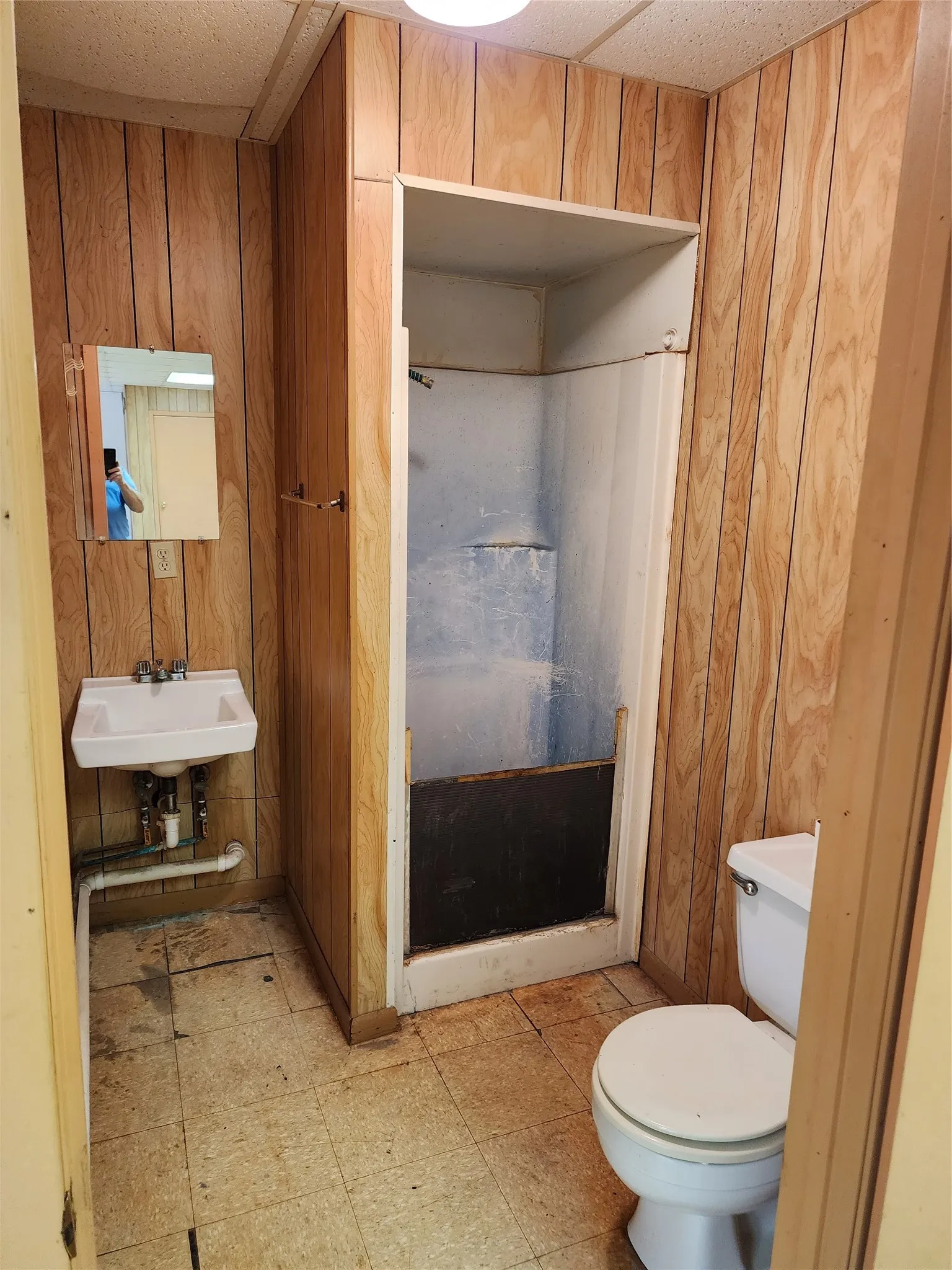 Bathroom featuring paneled walls, a wall-mounted sink, a toilet, and a shower stall