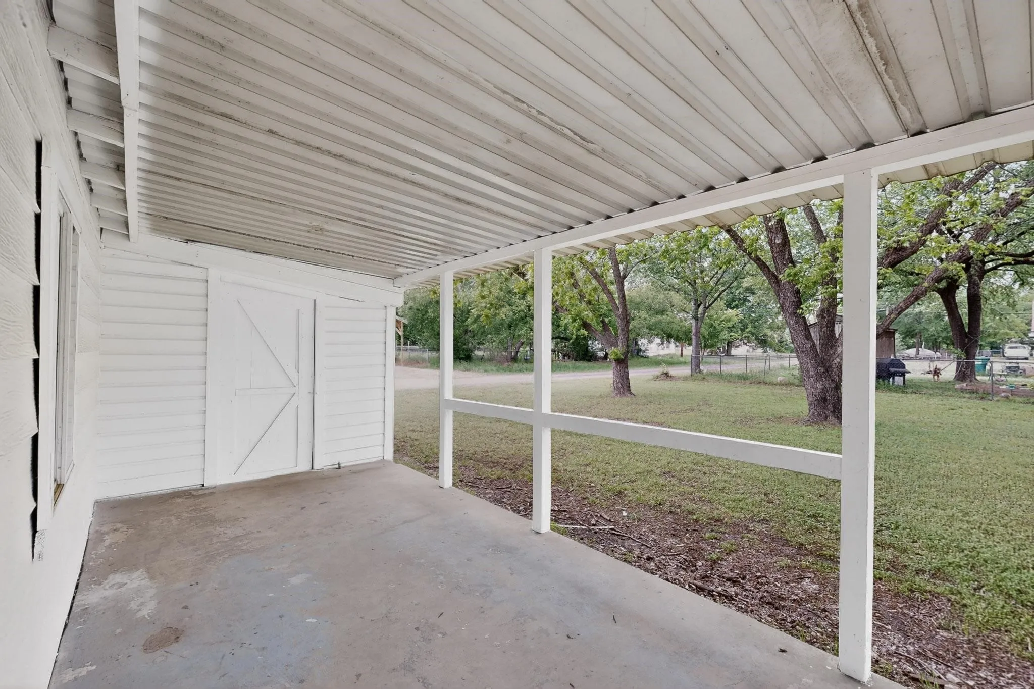 The back patio features a covered porch and a white barn-style door that leads to an attached shed.