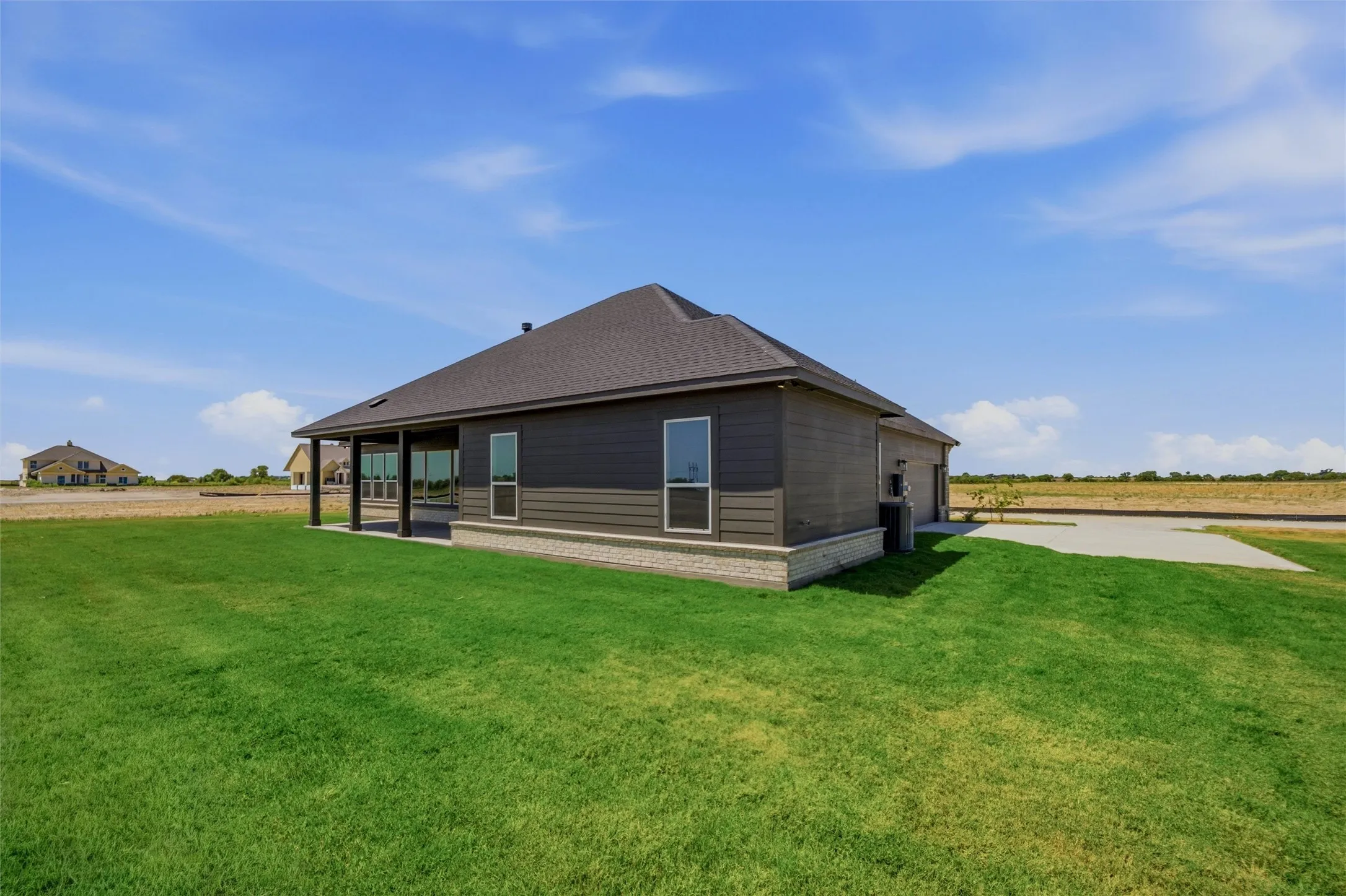 Spacious rear yard with a covered patio, concrete slab, and dark shingle roof