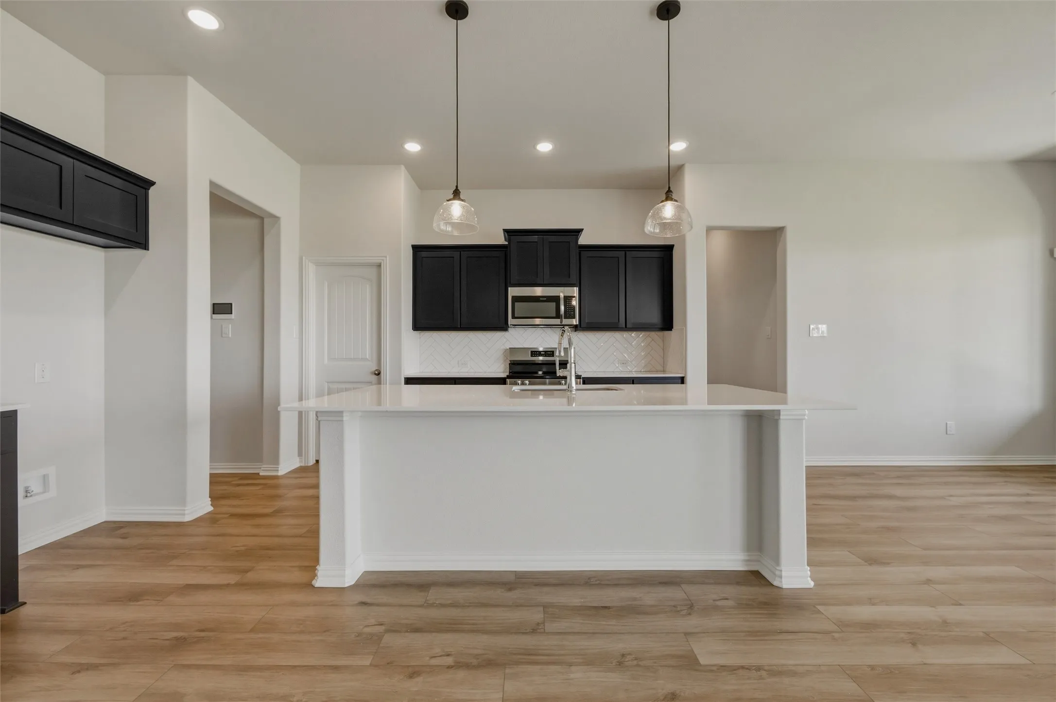 Kitchen featuring a large central island, dark cabinetry, stainless steel appliances, a white subway tile backsplash, and wood-finish flooring