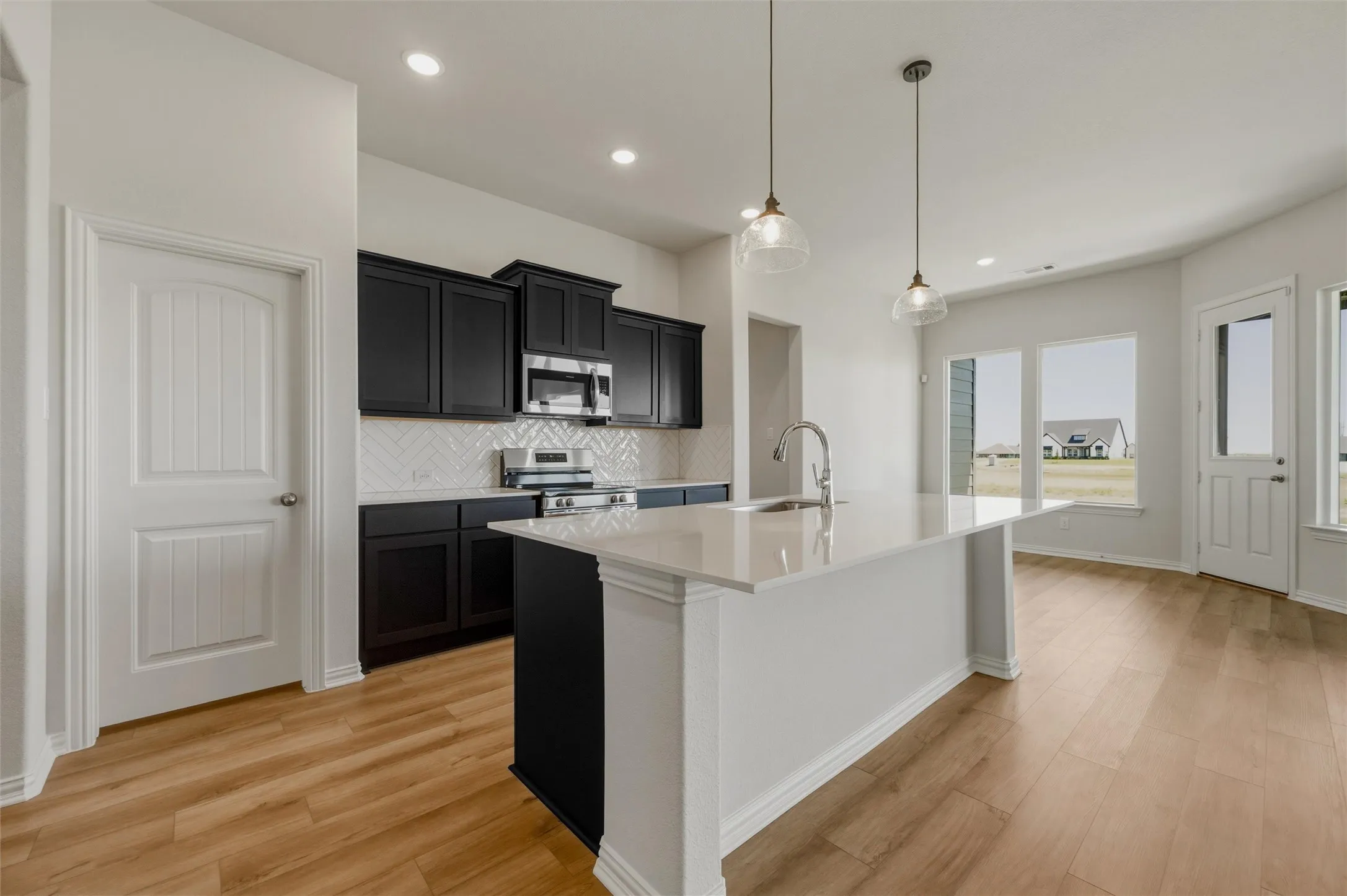 Open-concept kitchen with dark cabinetry, white herringbone tile backsplash, white countertop island, and wood-finish flooring
