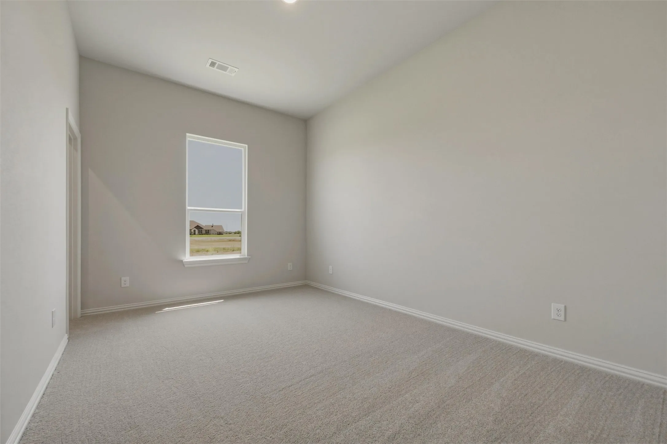Spacious room featuring neutral carpeting, light gray wall tones, a single window, and a vaulted ceiling