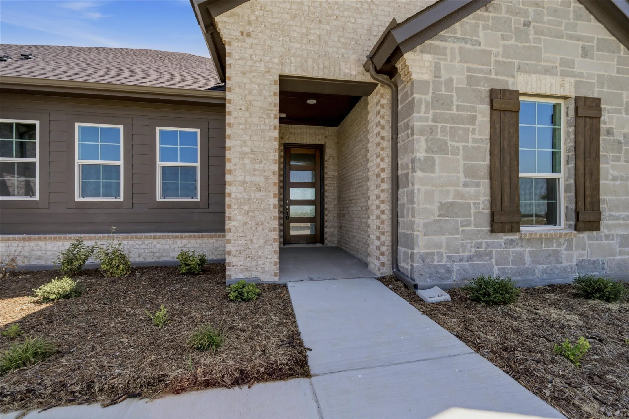 Exterior featuring a combination of brick and stone facade, a dark wood-finish entry door with frosted glass accents, and decorative window shutters