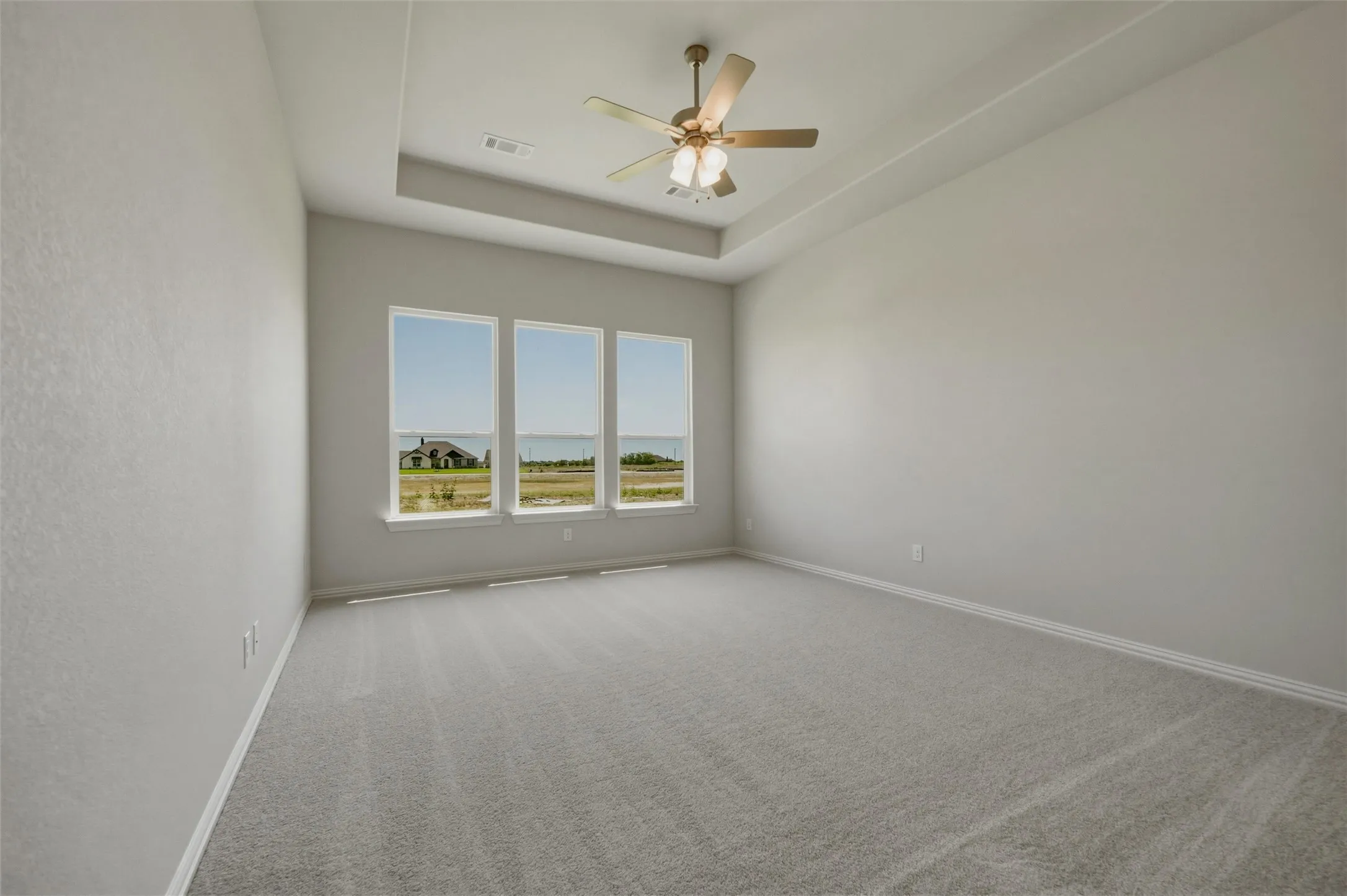 Recessed ceiling with an overhead fan, light gray carpeting, and three expansive windows