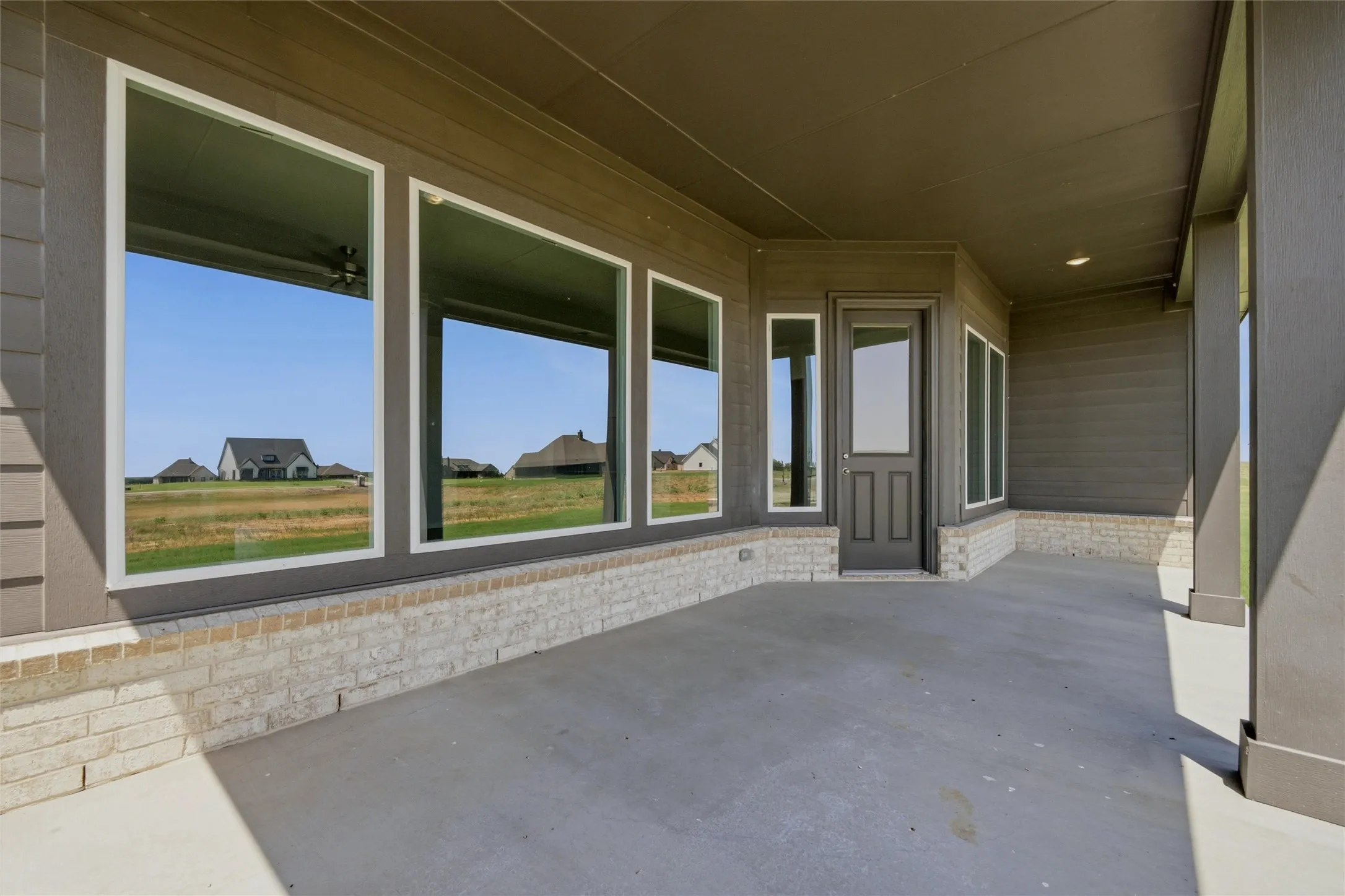 Covered patio with a concrete surface, stone base, multiple windows, and a panel door