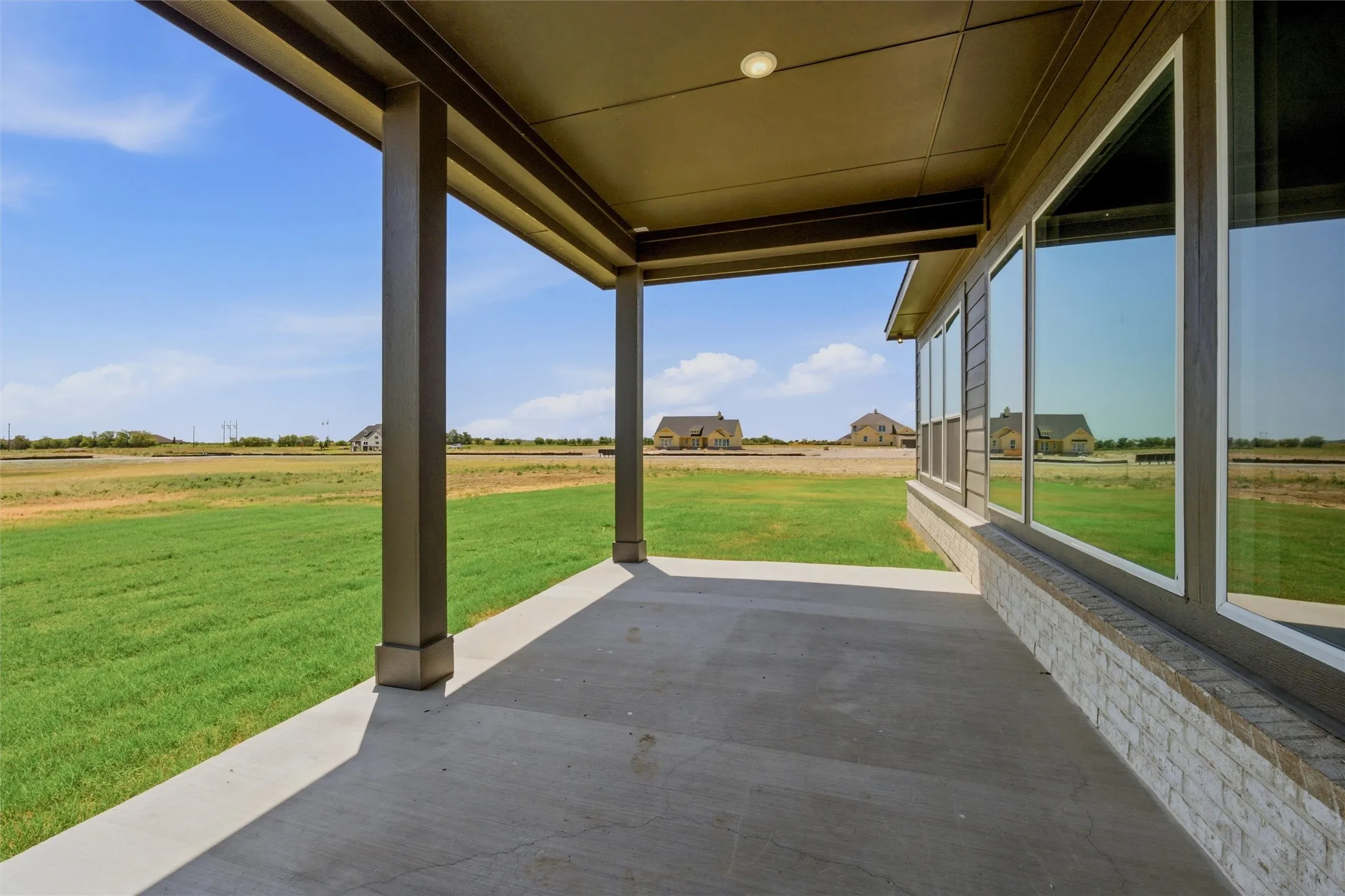Covered concrete patio with recessed lighting, offering an expansive lawn area