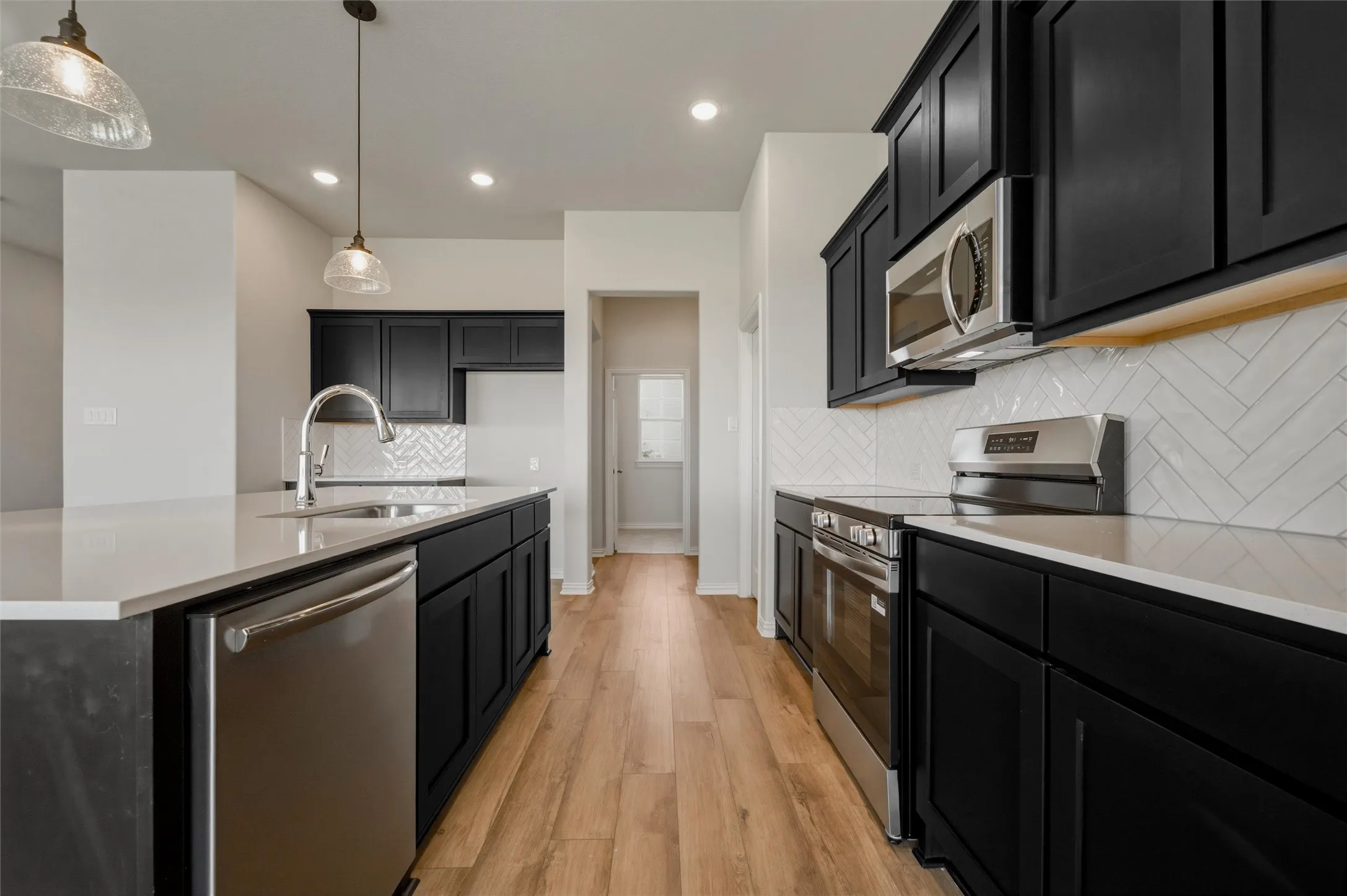 Kitchen featuring wood-finish flooring, dark cabinetry, light countertops, stainless steel appliances, and a herringbone tile backsplash