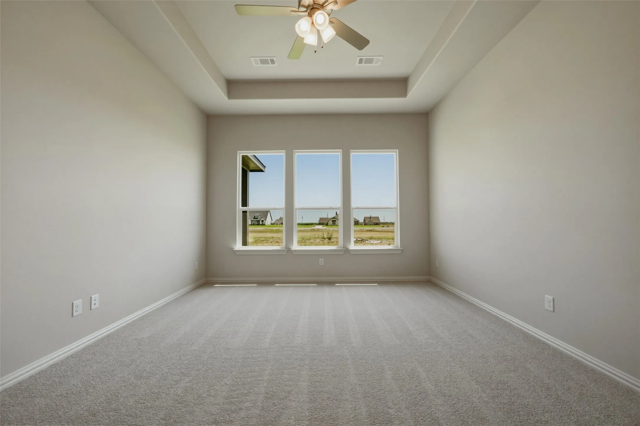 Spacious room with a tray ceiling, ceiling fan, carpet flooring, and three large windows