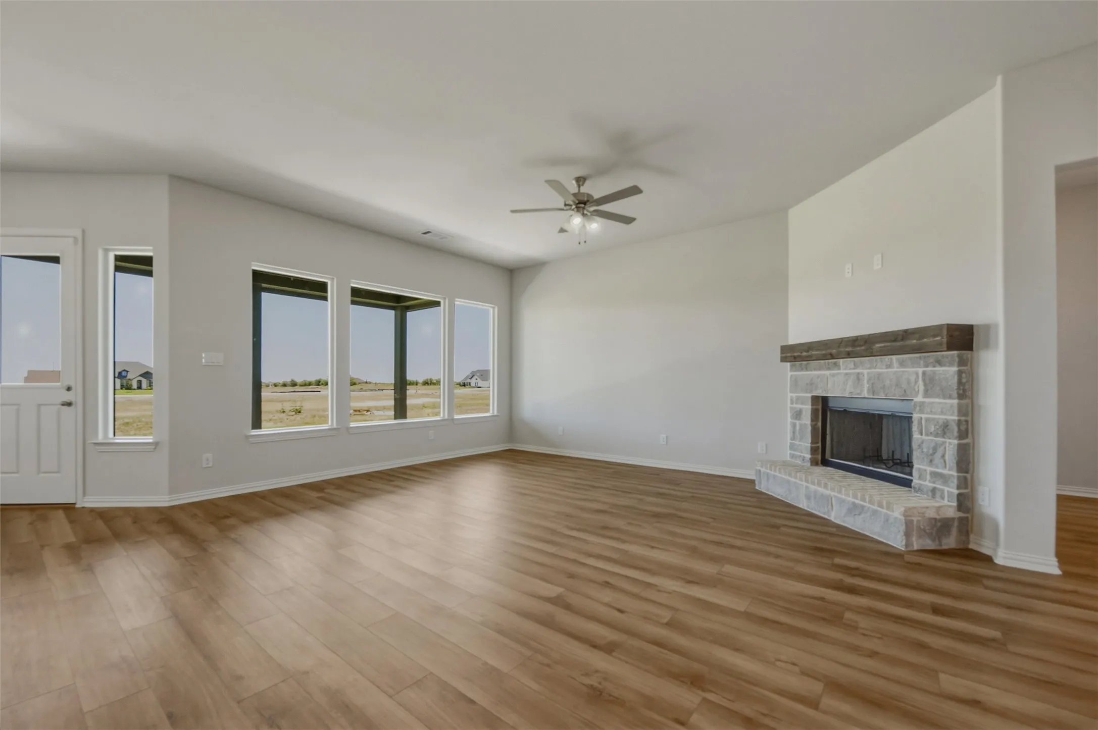 Spacious interior featuring wood-finish flooring, a stone fireplace with a wood mantle, and multiple windows