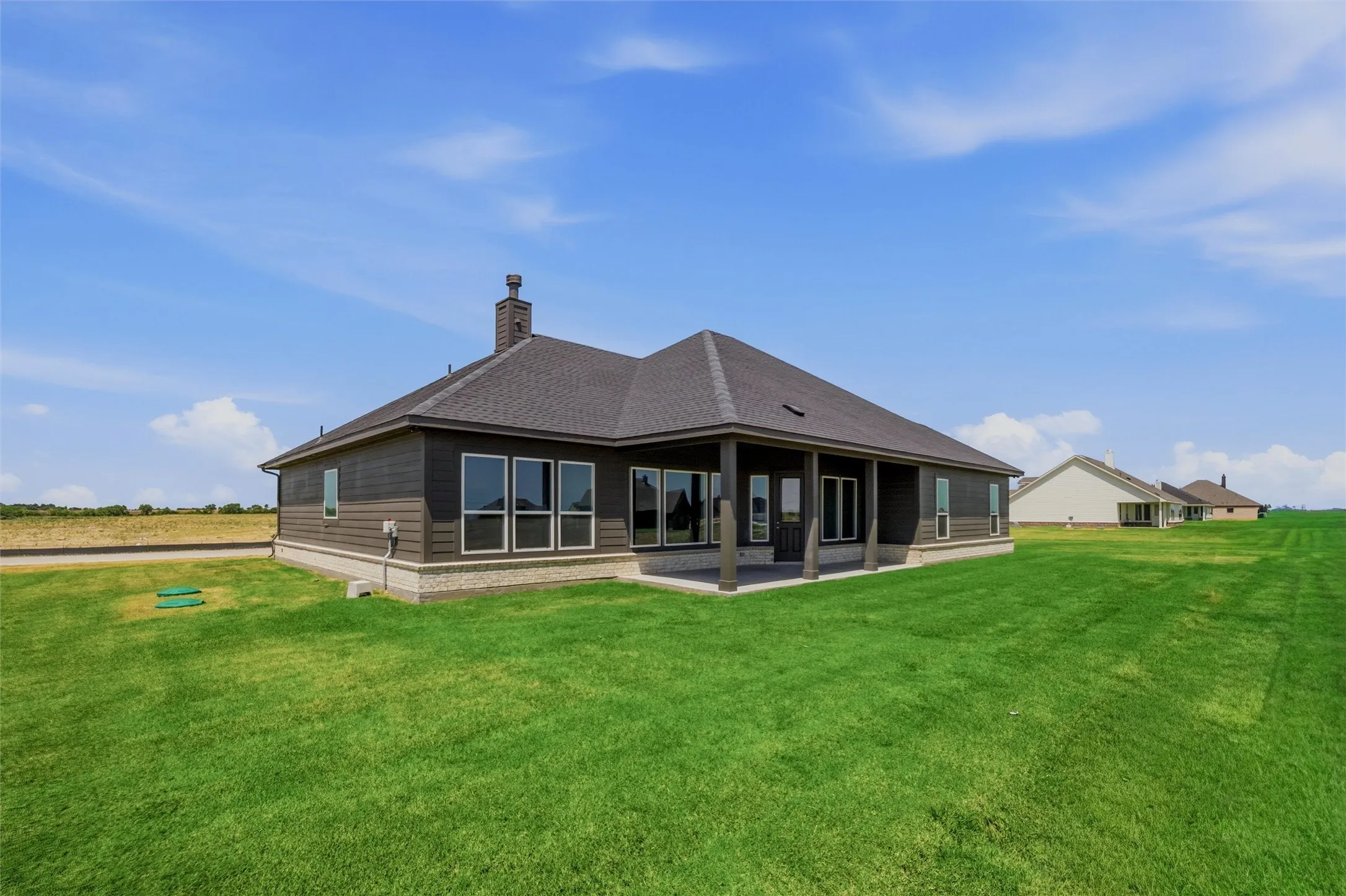 Rear exterior featuring a covered patio, multiple windows, dark siding, and a chimney