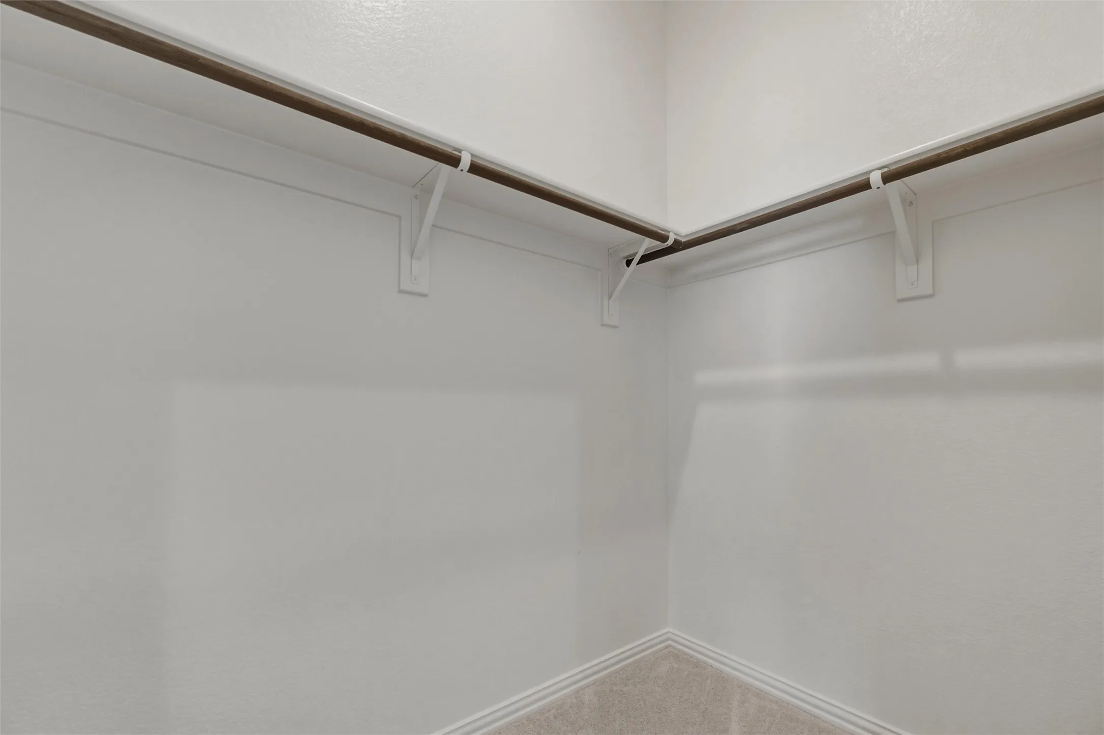 Corner closet with light-colored carpeting, white baseboards, and built-in clothes rods