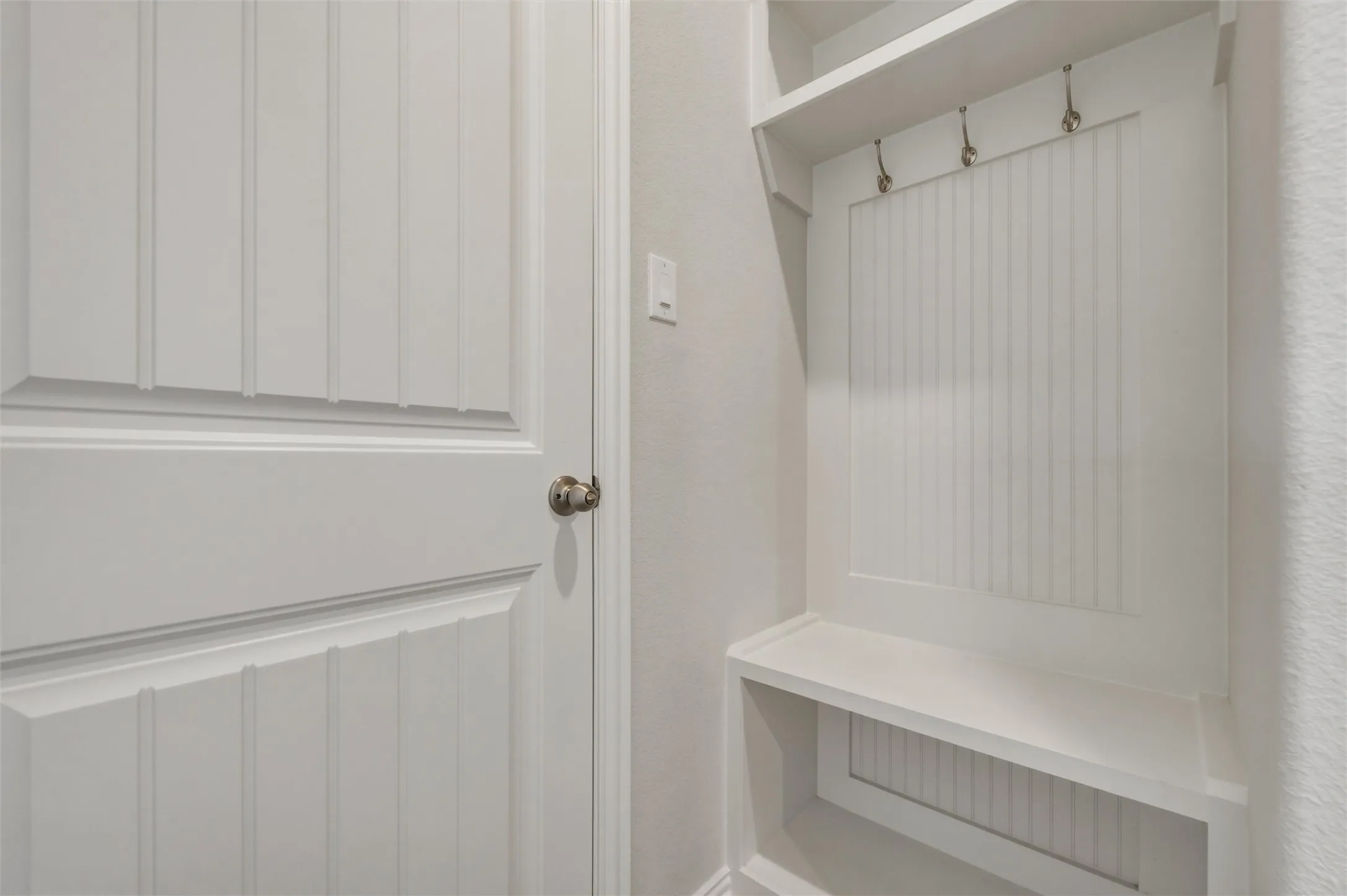 Built-in storage bench with beadboard backing, overhead shelving, and metal coat hooks