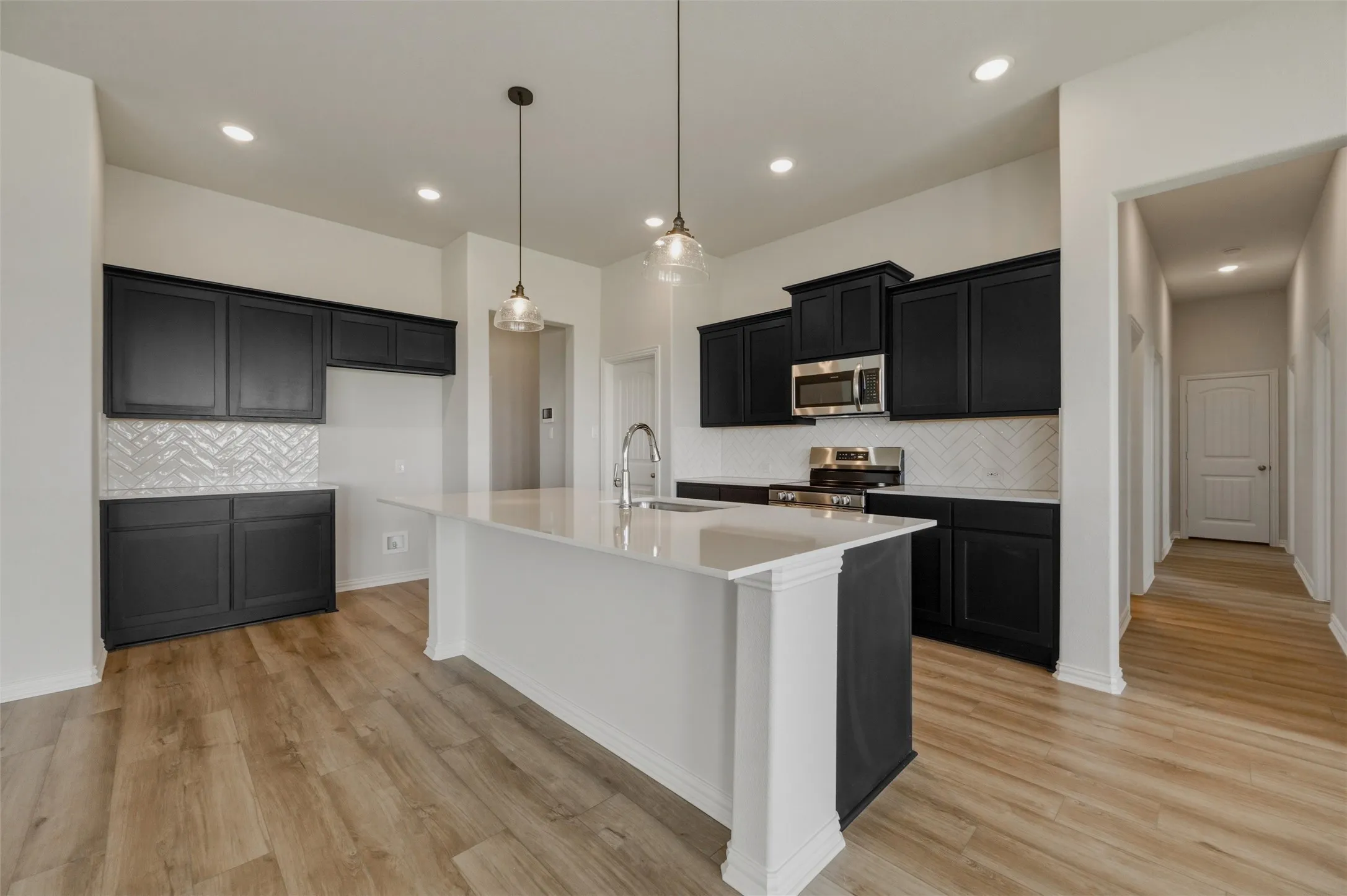 Kitchen featuring a central island, dark cabinetry, light countertops, a patterned tile backsplash, and wood-finish flooring